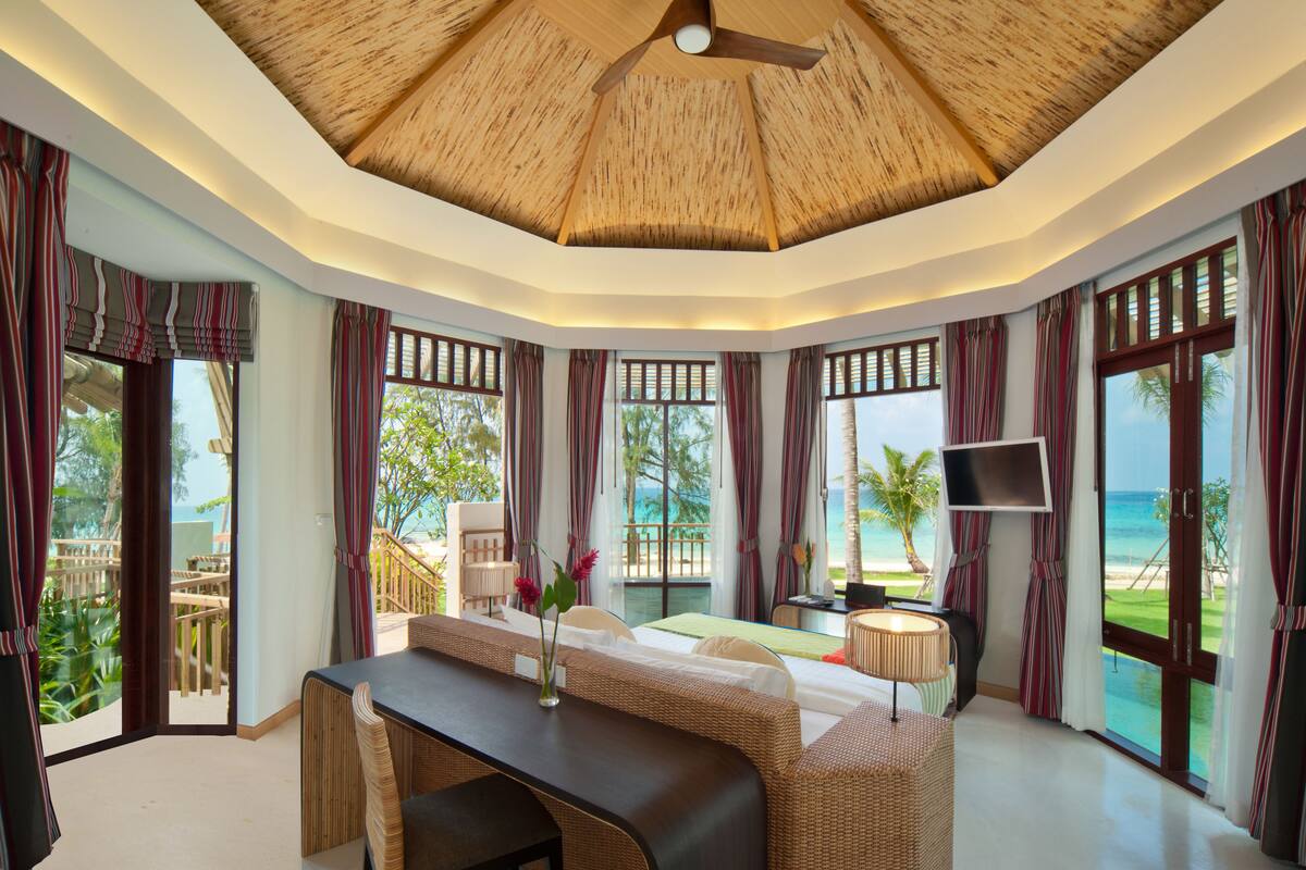 A room with a ceiling fan, large windows, a bed, a desk, and a TV.