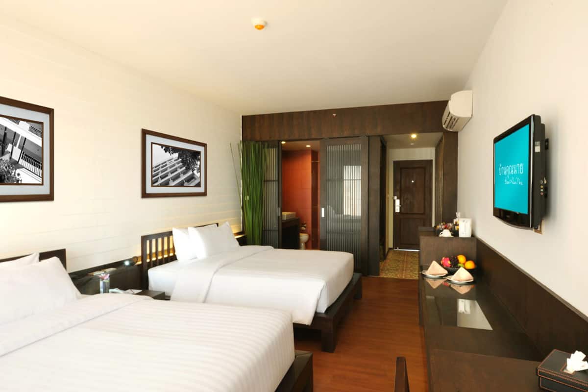 Habitación de hotel con dos camas, un escritorio, un televisor y cuadros en la pared.