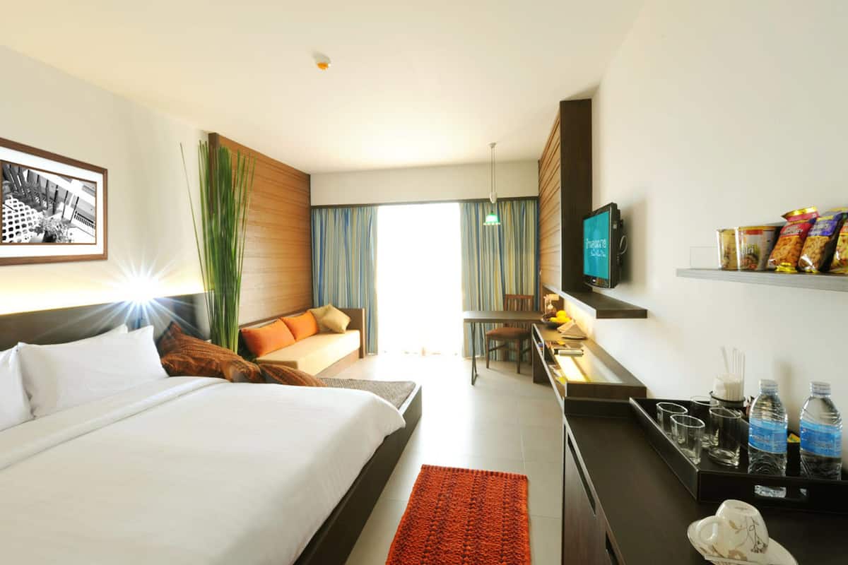 Habitación de hotel con cama, escritorio, televisión y estante con aperitivos.