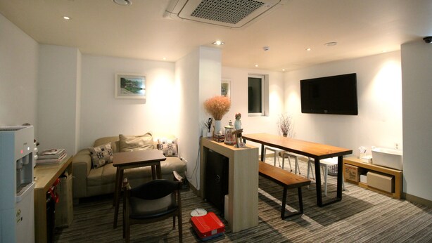 A compact living space with a sofa, a dining table, a TV mounted on the wall, and a kitchenette area. - Hotel Irene City (Seoul)