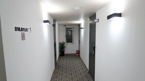A hallway with a carpeted floor, a potted plant, a fire extinguisher, and a door with a sign. - Hotel Irene City (Seoul)