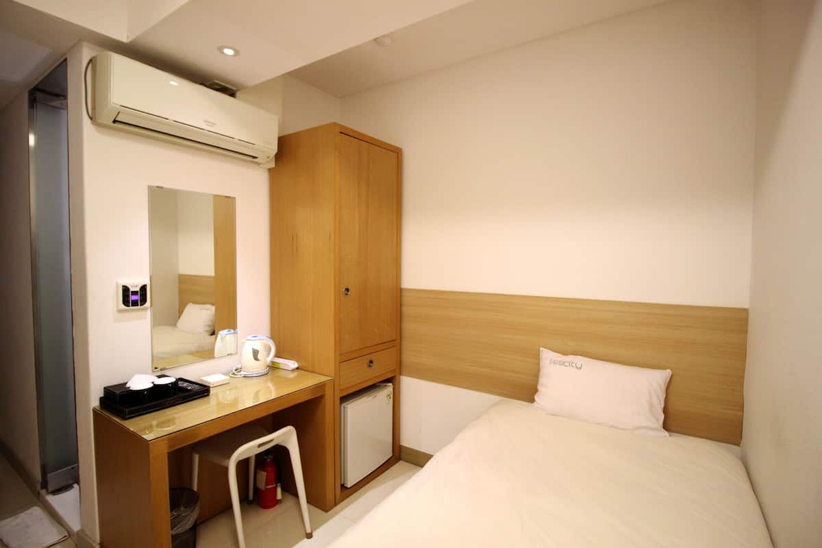 Habitació d'hotel amb un llit, un escriptori de fusta amb una cadira, un refrigerador petit, un mirall i un aparell d'aire condicionat.