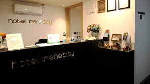 A hotel reception desk with a sign reading "hotel irenecity," a clock, framed certificates, and a vase of flowers. - Hotel Irene City (Seoul)