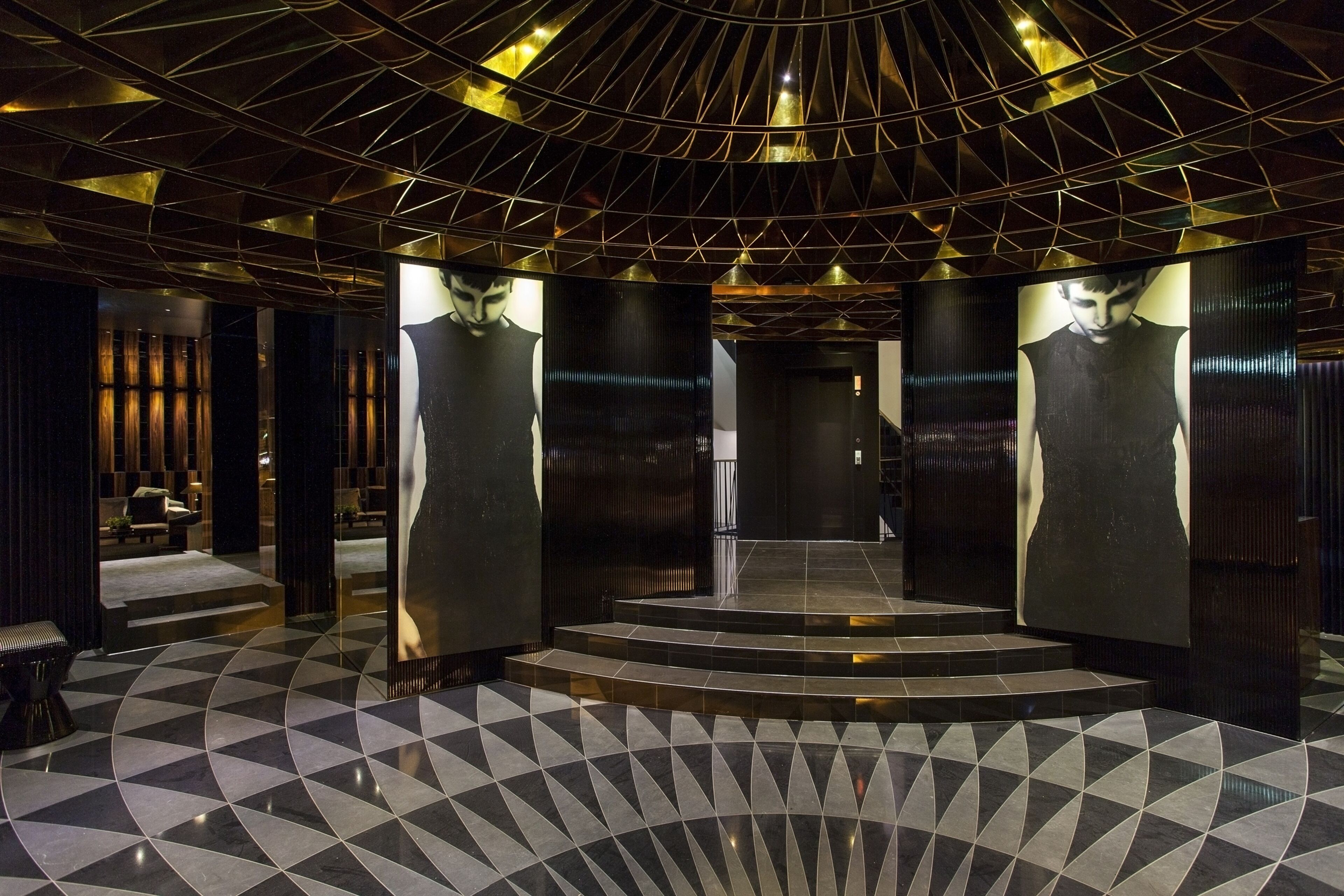 Un vestíbulo moderno con piso estampado con motivos geométricos, una escalera central y un techo con diseño geométrico.