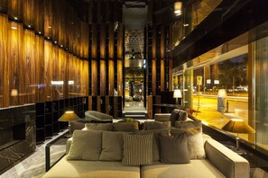 A modern lobby with a sofa, lamps, and a view of the street outside.