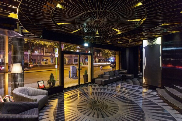 A modern lobby with a geometric floor pattern, seating area, and a large glass wall offering a view of the street. - Quentin Boutique Hotel (Berlin)