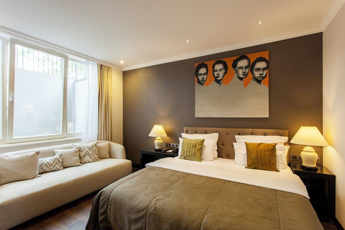 A hotel room with a large bed, a sofa, two bedside tables with lamps, and a window with curtains.