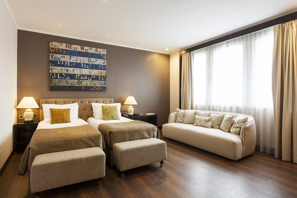 A hotel room with two beds, a sofa, and a large window with curtains.