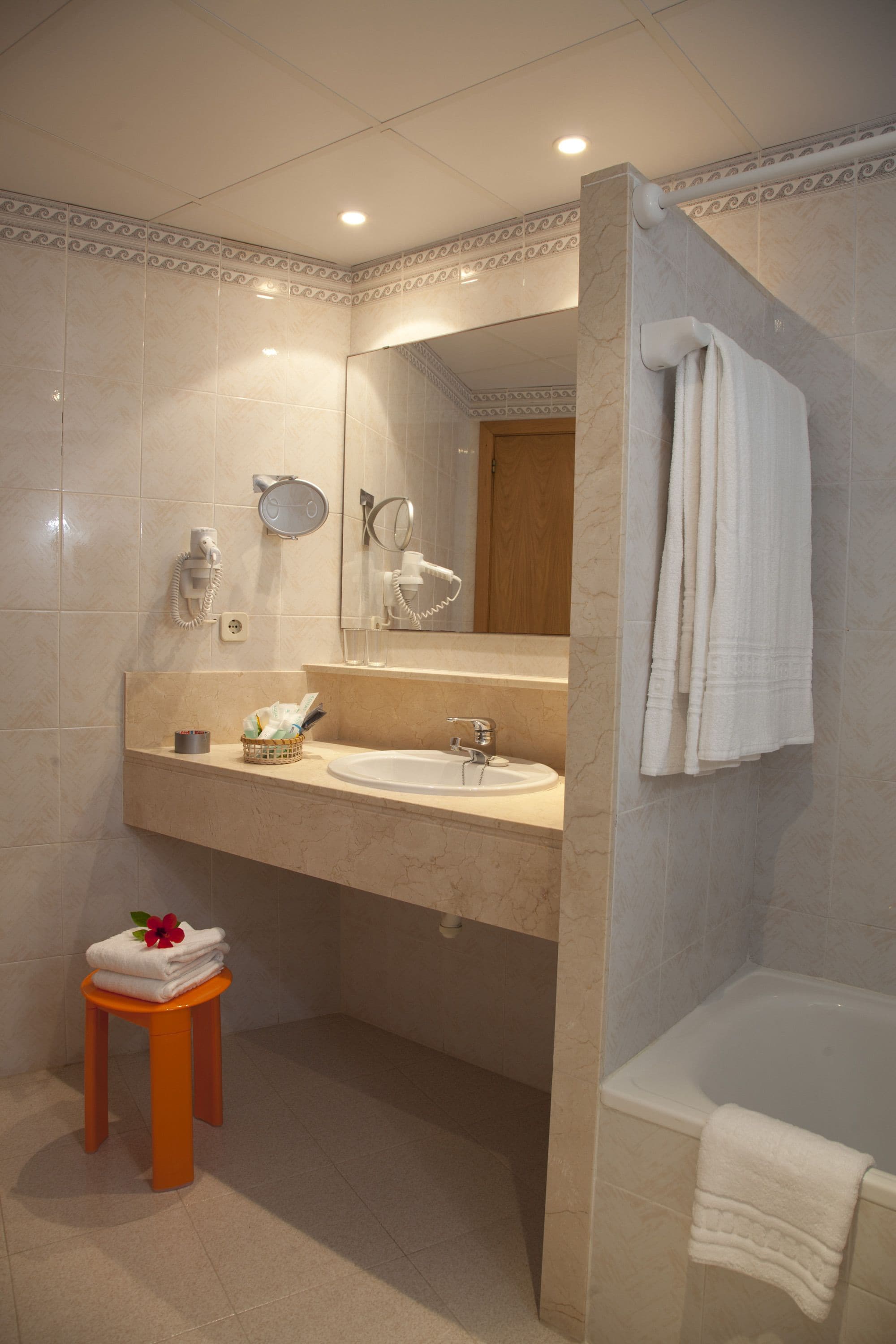 Un baño con lavamanos de mármol, un espejo, toallero, un taburete pequeño con toallas y una bañera.