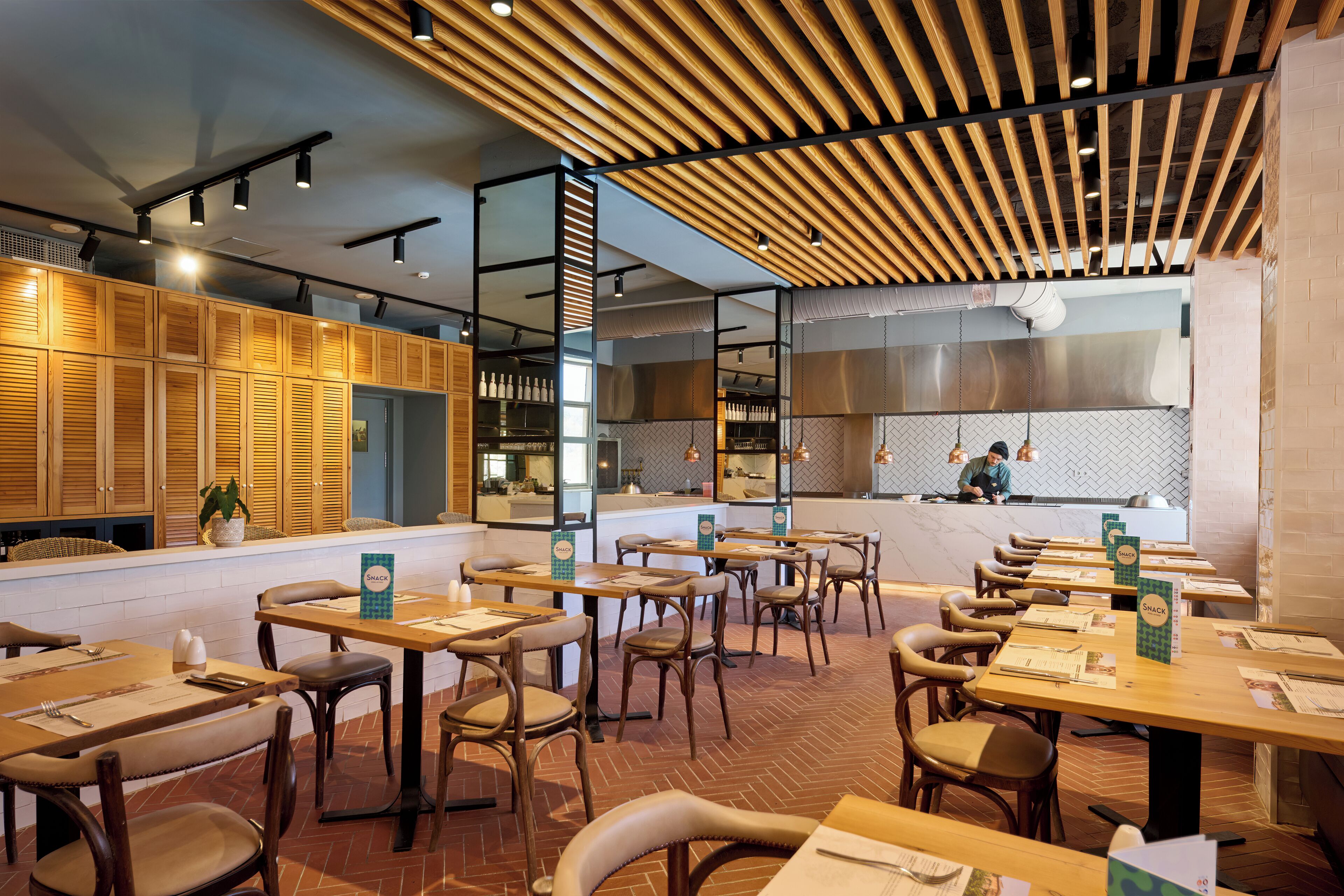 Un restaurant avec des murs lambrissés, un sol en briques et une cuisine visible au fond de la salle.