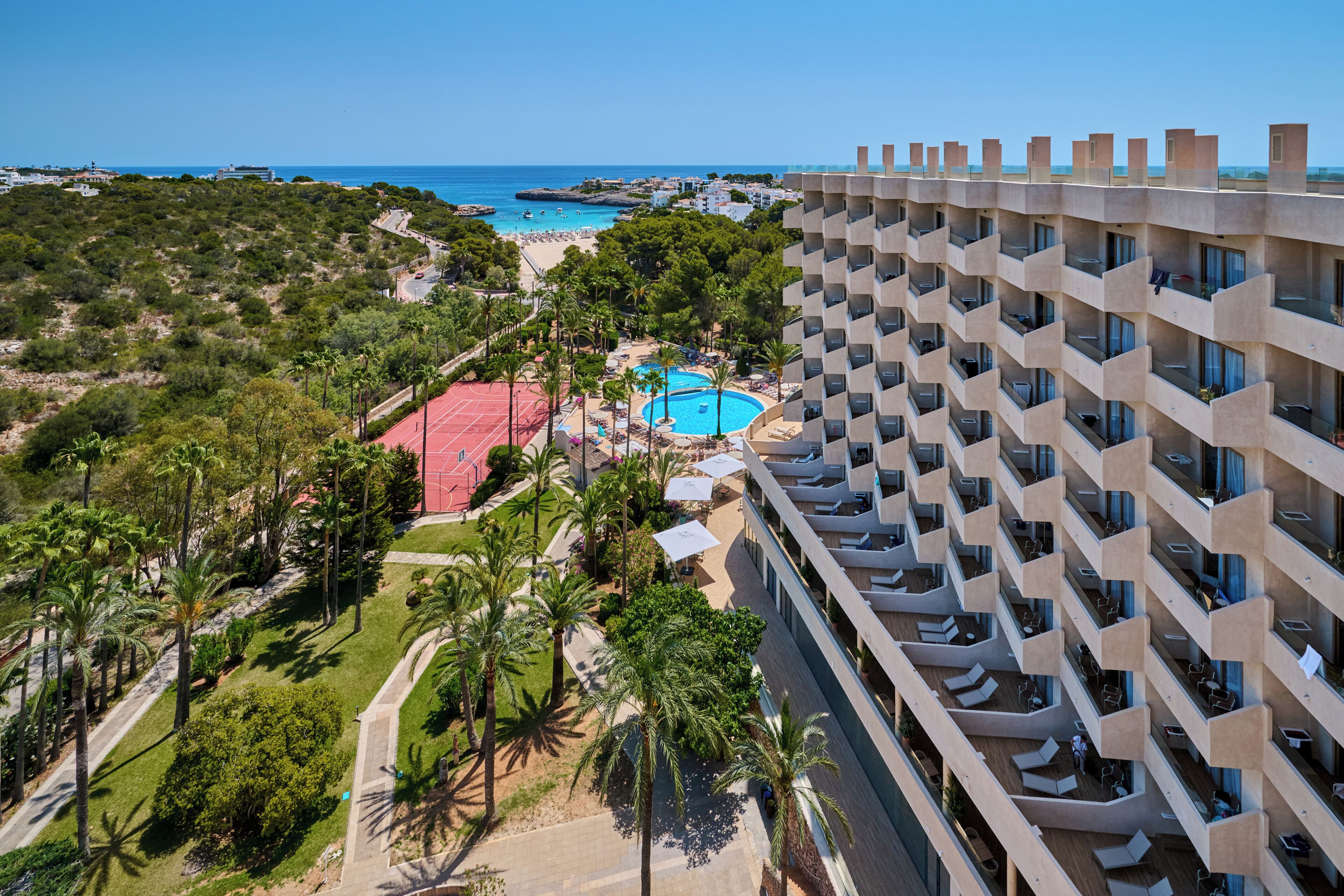 A high-rise hotel with a swimming pool, palm trees, and a view of the beach.