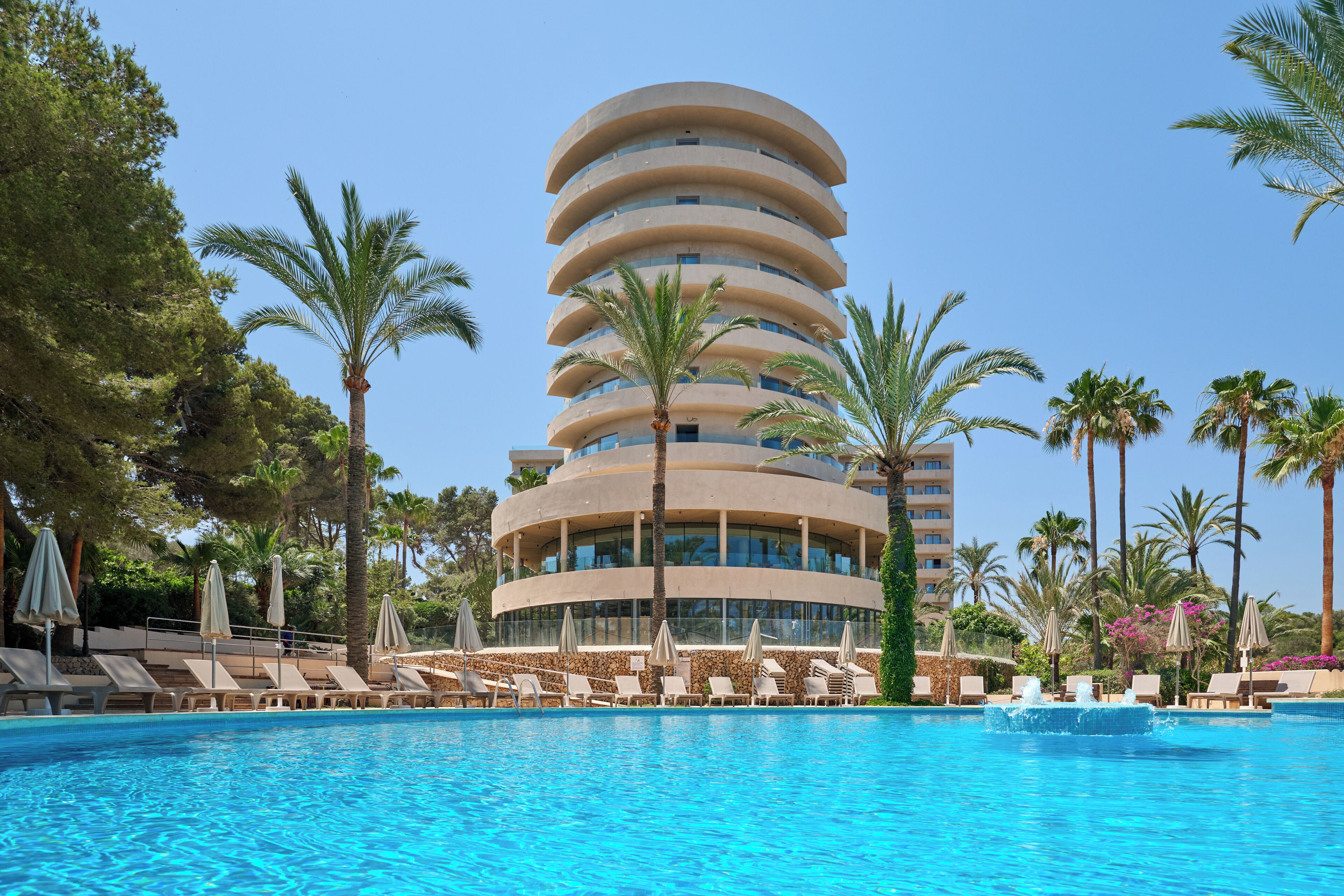 Un hotel moderno dal design circolare, con piscina, lettini e palme.