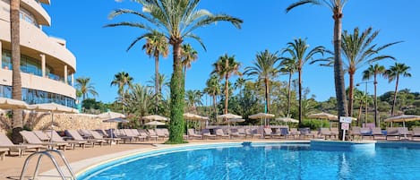 Zona de piscina con sillones de descanso y palmeras.