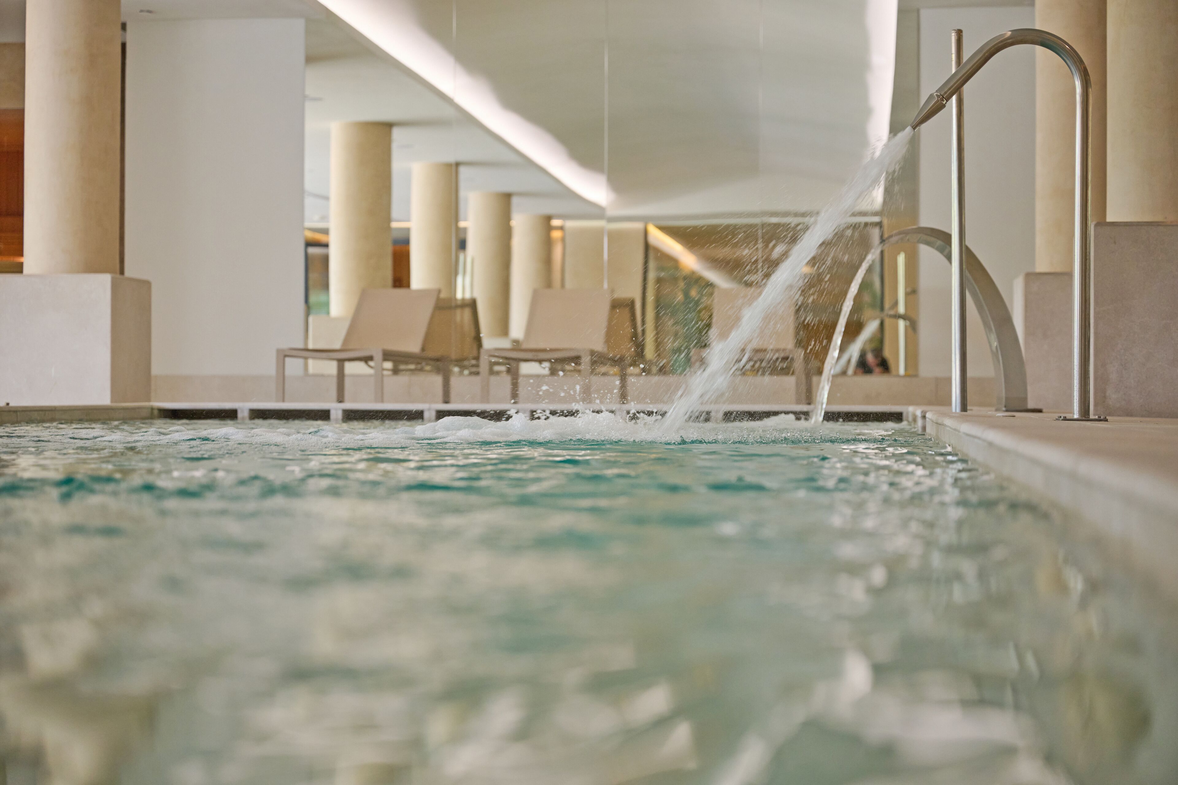 A pool area with a water feature, lounge chairs, and a modern architectural design.