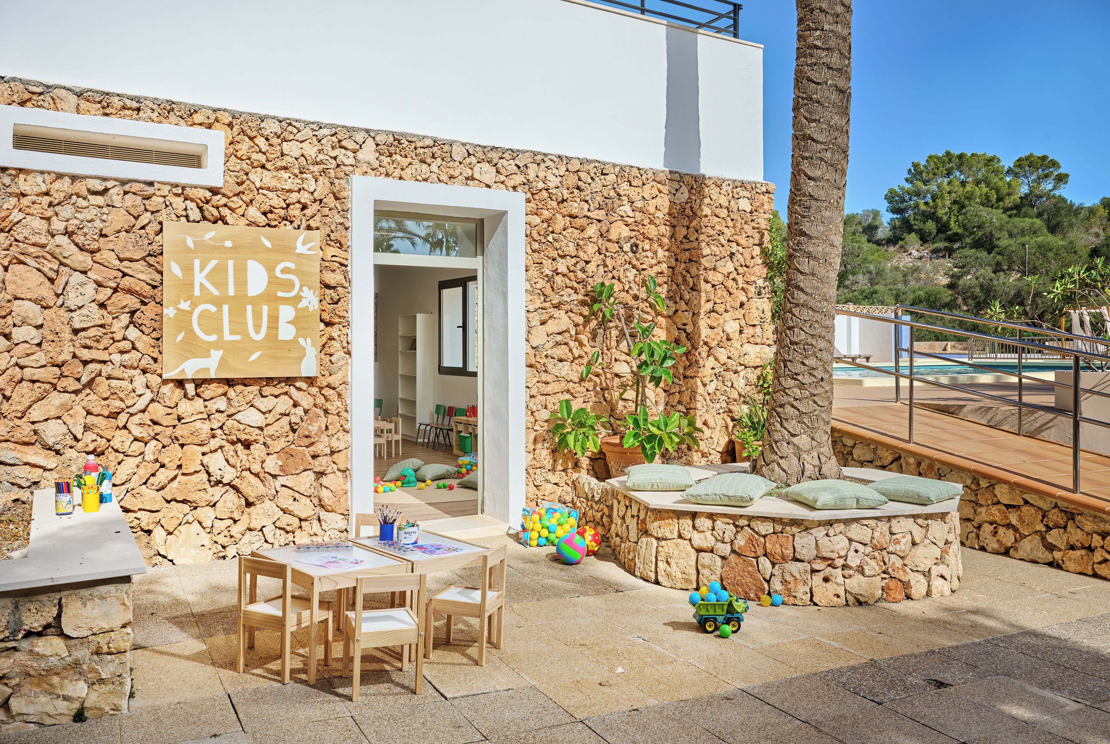 A stone building with a sign reading 'KIDS CLUB' and a play area with toys and a table.