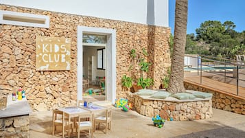 A stone building with a sign reading 'KIDS CLUB' and a play area with toys and a table.