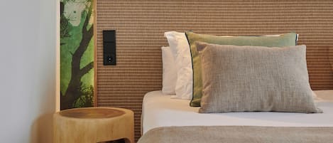 A neatly made bed with a textured headboard, a small wooden stool, and a wall-mounted light fixture.