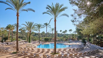 A resort pool area with multiple lounge chairs and umbrellas, surrounded by palm trees.