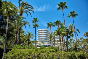 Een hotel met meerdere verdiepingen en een rond ontwerp, omringd door palmbomen en groen.