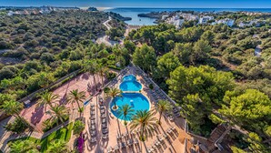 Vista aérea de un resort con varias piscinas, palmeras y un telón de fondo costero.