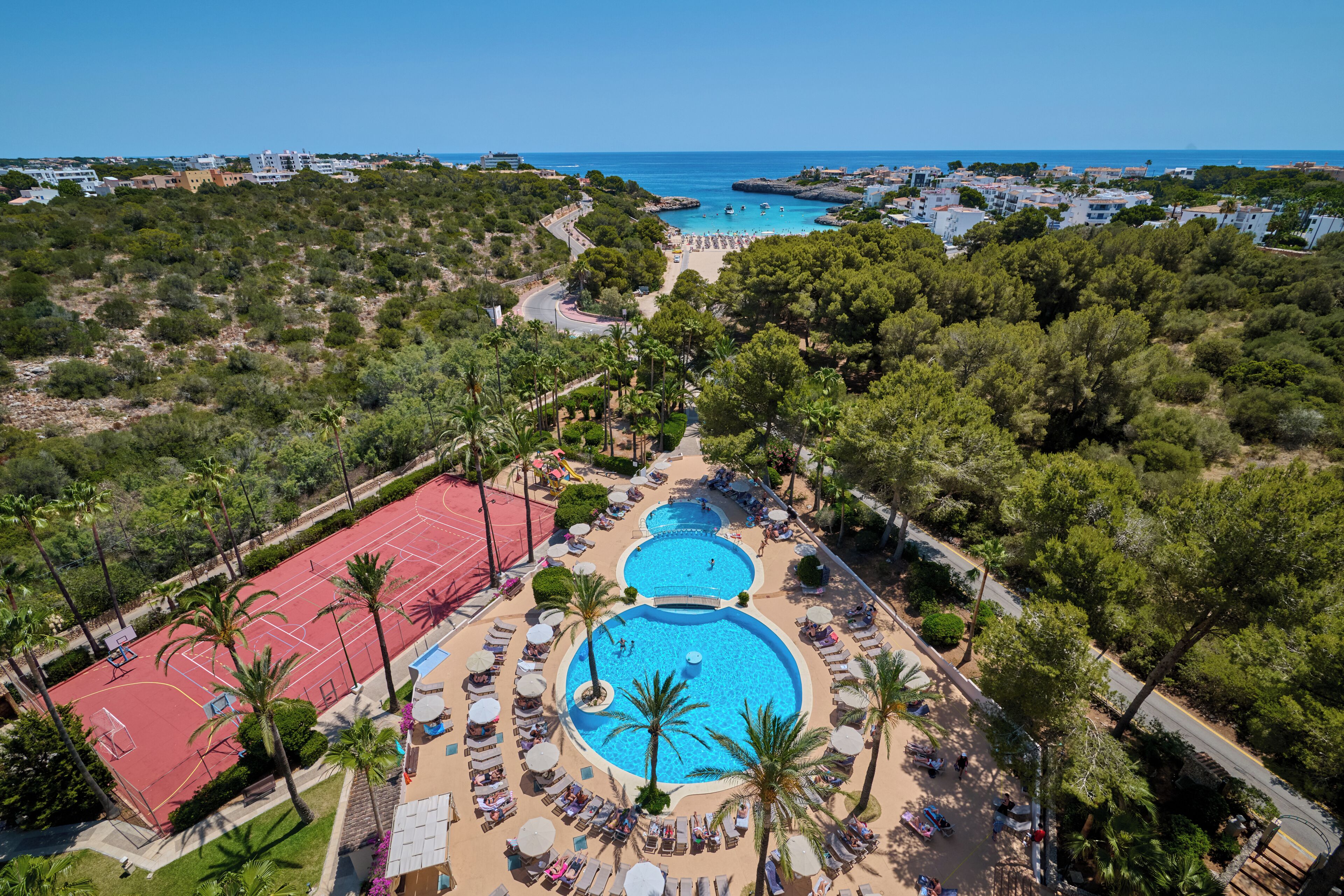 Un resort con varias piscinas, cancha de tenis y vista al mar.