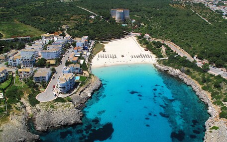 An aerial view of a coastal area with a sandy beach, clear blue waters, and a residential area with buildings.