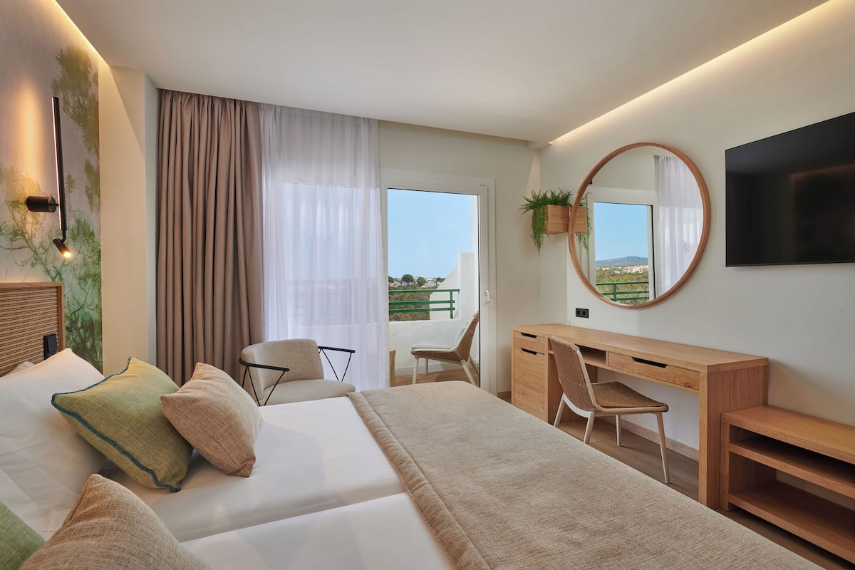 Een moderne hotelkamer met een bed, bureau, stoel, televisie en balkon met uitzicht.