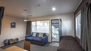 A room with a bed, a sofa, a table, a ceiling fan, and a window with curtains. - Landmark Manor Motel (New Plymouth)
