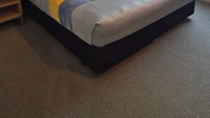 A hotel room with a large bed, a wooden headboard, a bedside table, and a window with curtains. - Landmark Manor Motel (New Plymouth)