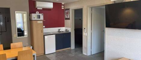 Una habitación de hotel compacta con kitchenette, un comedor con sillas, un ventilador de techo y un televisor de pantalla plana.