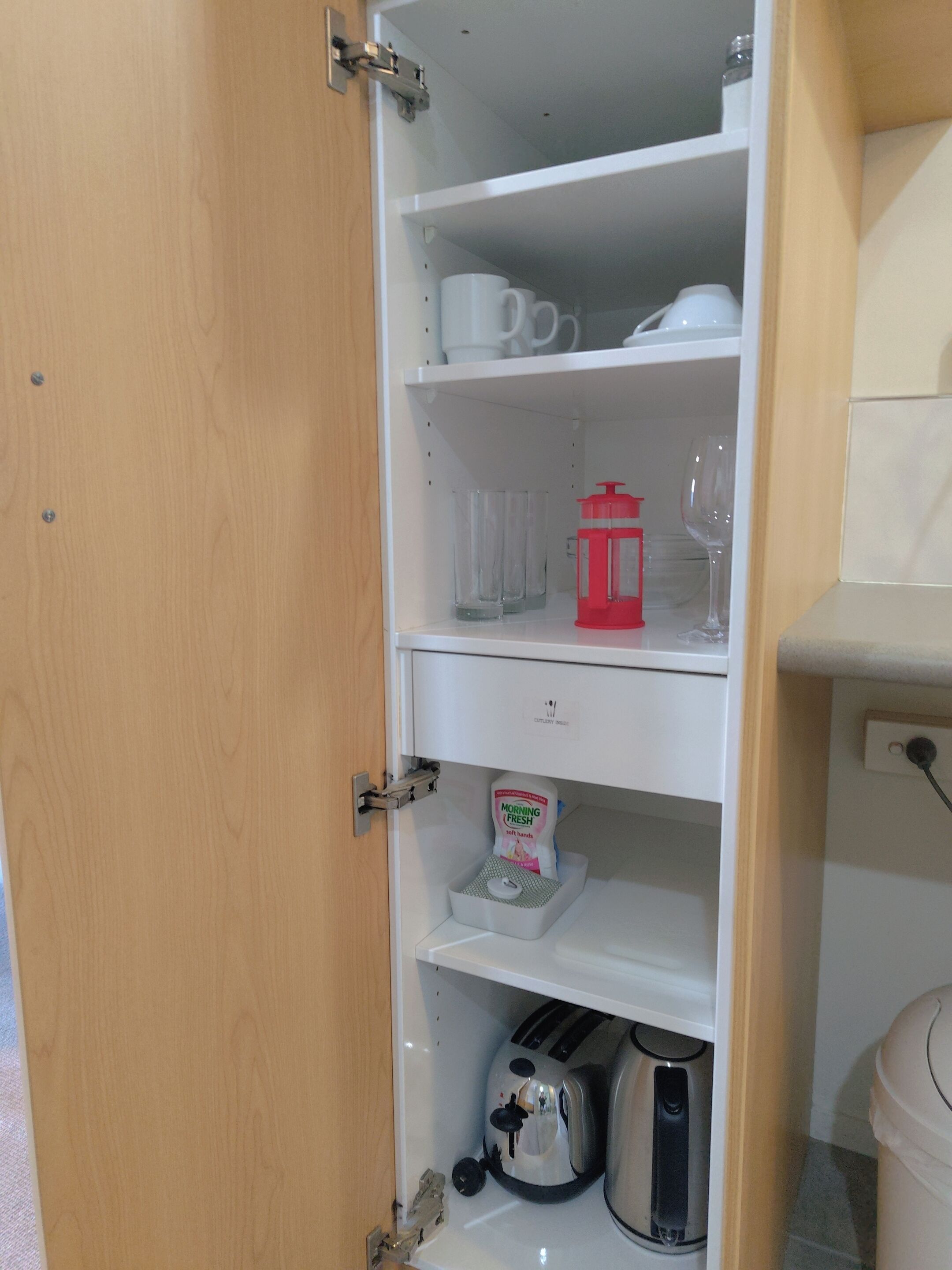 Una cocina con un mueble blanco que contiene una cafetera, un tostador y un hervidor.