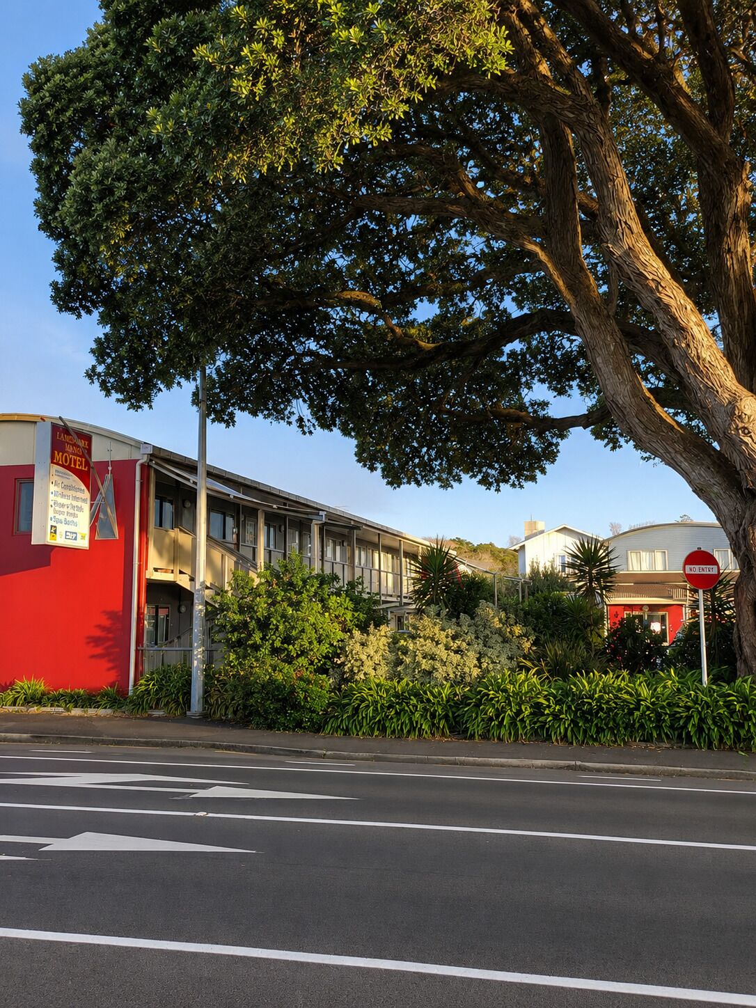 A motel with a red facade, a large tree in front, and a 'No Entry' sign.