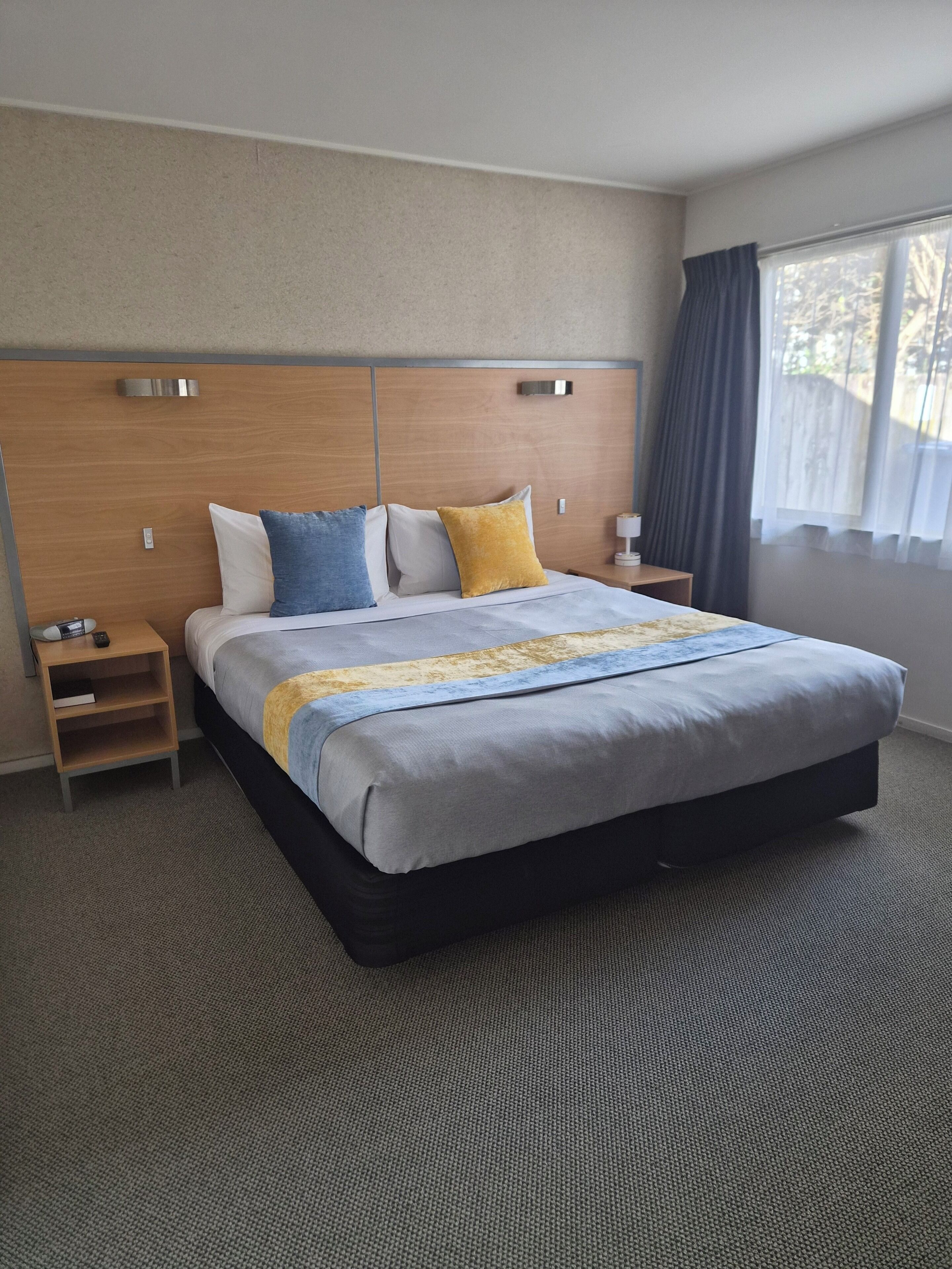 Quarto de hotel com uma cama grande, cabeceira de madeira, mesas de cabeceira e vista para o exterior.