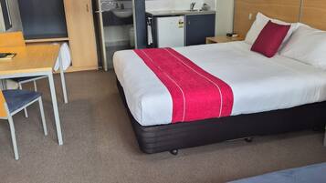 A hotel room with a bed, a desk, a chair, a microwave, a sink, and a ceiling fan.