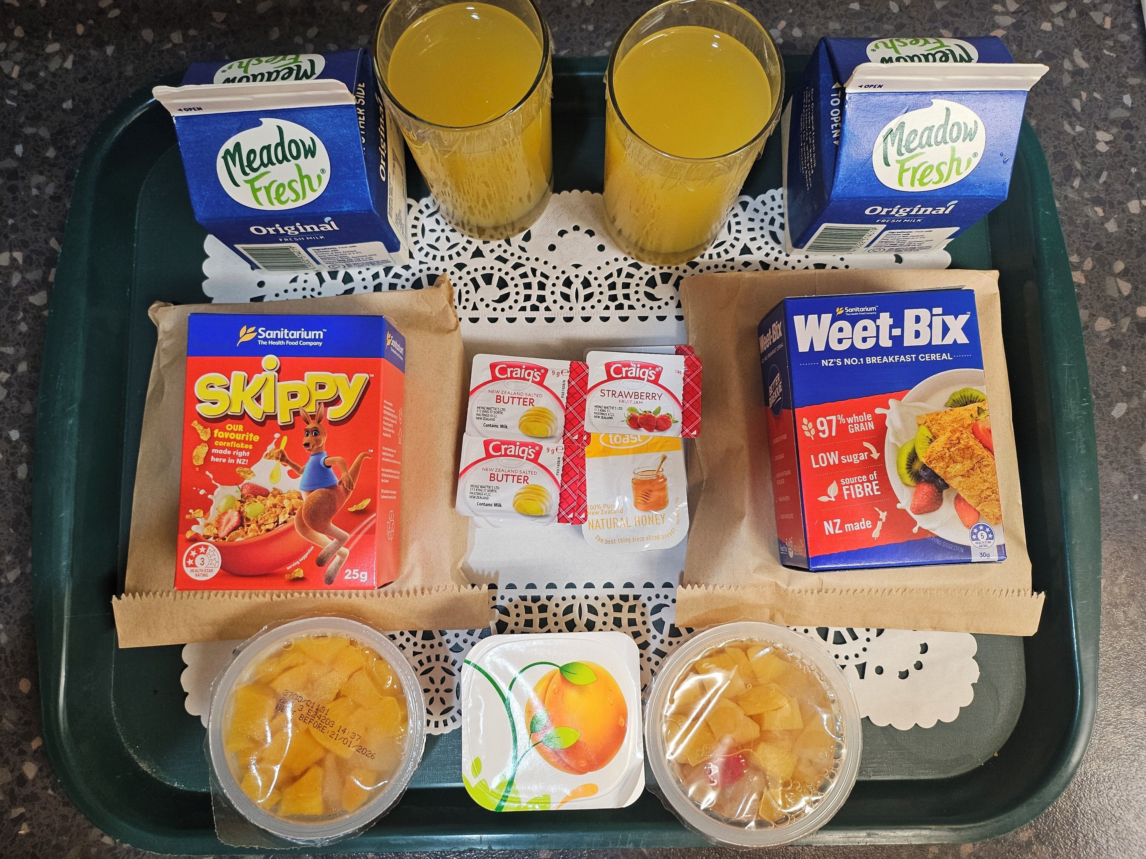 A tray with Meadow Fresh milk cartons, Skippy cereal, Weet-Bix, and two fruit containers.