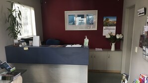 A reception area with a blue counter, a potted plant, a framed picture, and a calendar on the wall. - Landmark Manor Motel (New Plymouth)