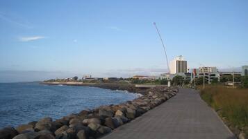 A coastal walkway with a concrete path, a rocky breakwater, and buildings in the background.