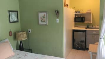 Une chambre de taille modeste, équipée d’un lit, d’un bureau, d’un four à micro-ondes et d’un petit réfrigérateur.