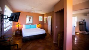 Un dormitorio con cama, dos lámparas de noche, ventilador de techo, televisor montado en la pared y una ventana con persianas.