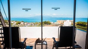 Un balcón con dos sillas y una mesa, con vistas a la costa, edificios y un cielo despejado.