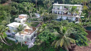 Un edificio de varios pisos con piscina, rodeado de exuberante vegetación y palmeras.