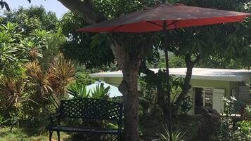 A garden with a bench, a red umbrella, and a tree.