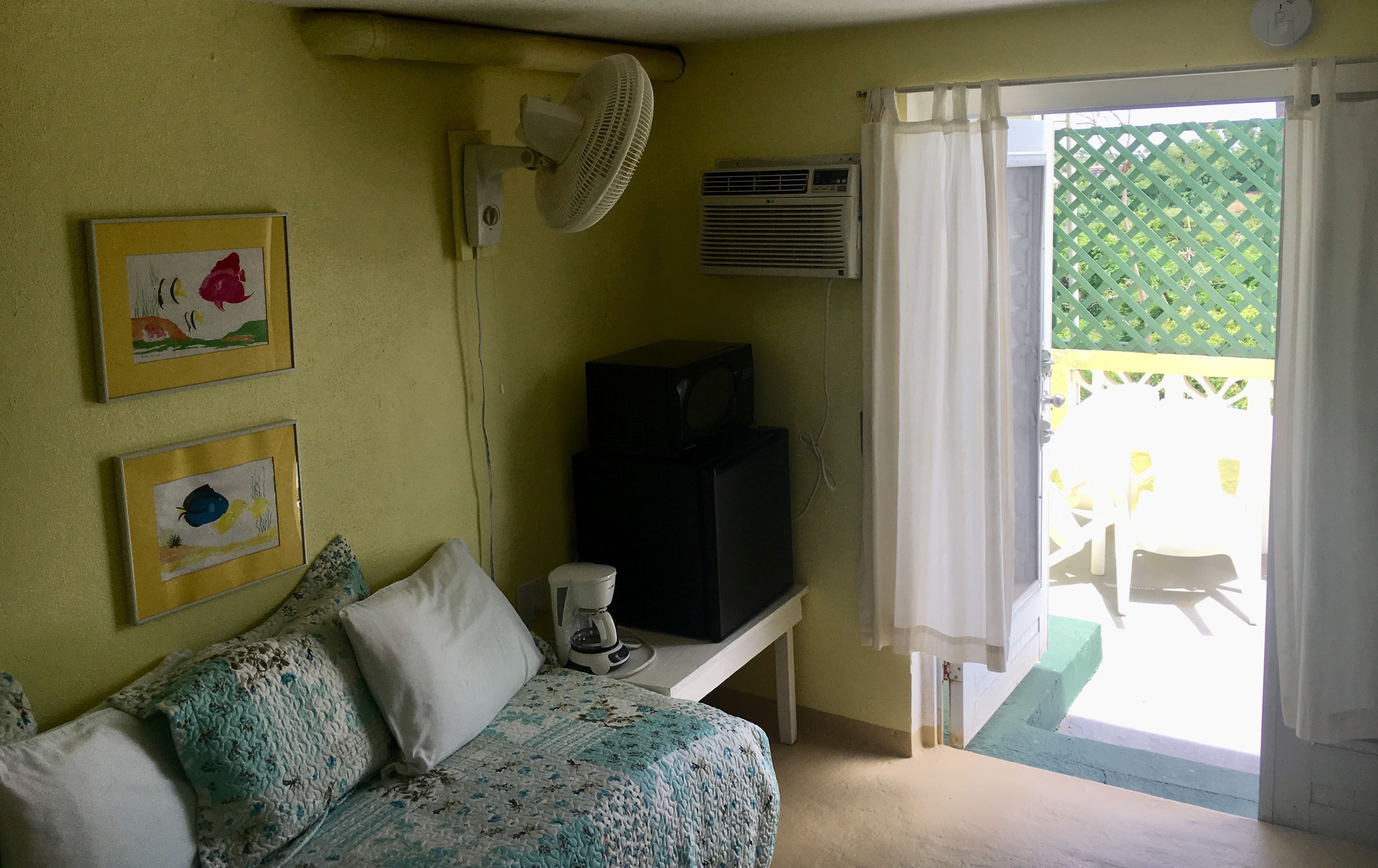A room with a bed, a ceiling fan, an air conditioner, and a view of an outdoor patio.