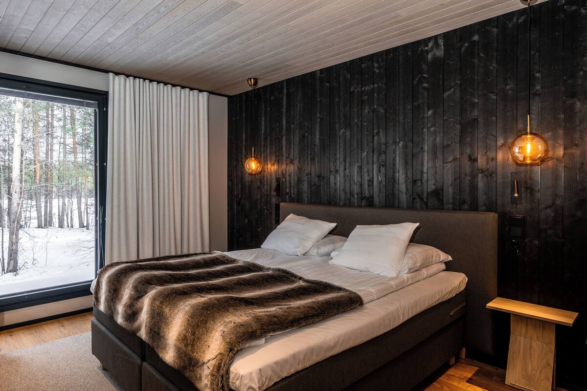 Ein modernes Schlafzimmer mit einem großen Bett, einer Holzwand und einem Fenster mit Blick auf Bäume.