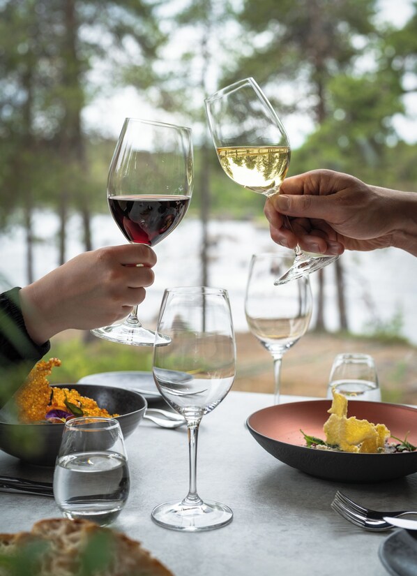 A dining table with wine glasses, a bowl of food, and a view of trees and water. - Wilderness Hotel Juutua (Inari)