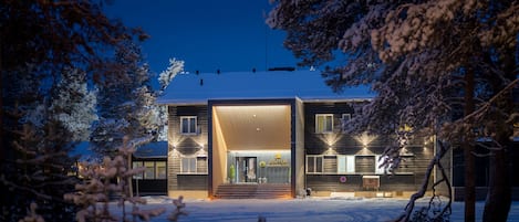 Un edificio moderno con facciata in legno, un'ampia entrata e un cartello con la scritta 'JuTua Wilderness Hotel'.