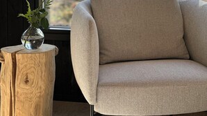 Ein Zimmer mit einem beigefarbenen Sessel, einem Holzbalken und einer Vase mit einer Blume.