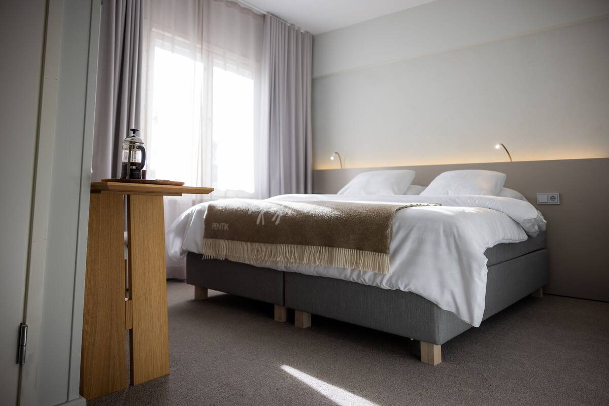 Ein modernes Hotelzimmer mit einem Bett, einem Holztisch und einem Nachttisch.