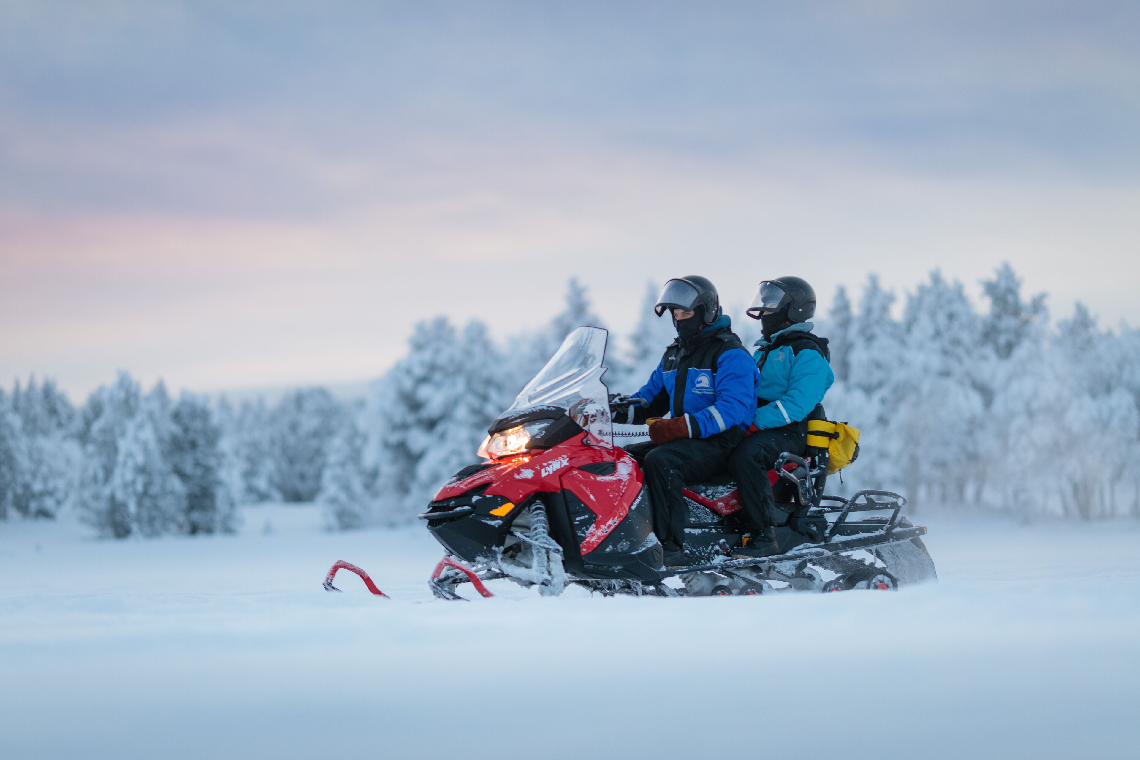A snowmobile with two riders in a snowy landscape.