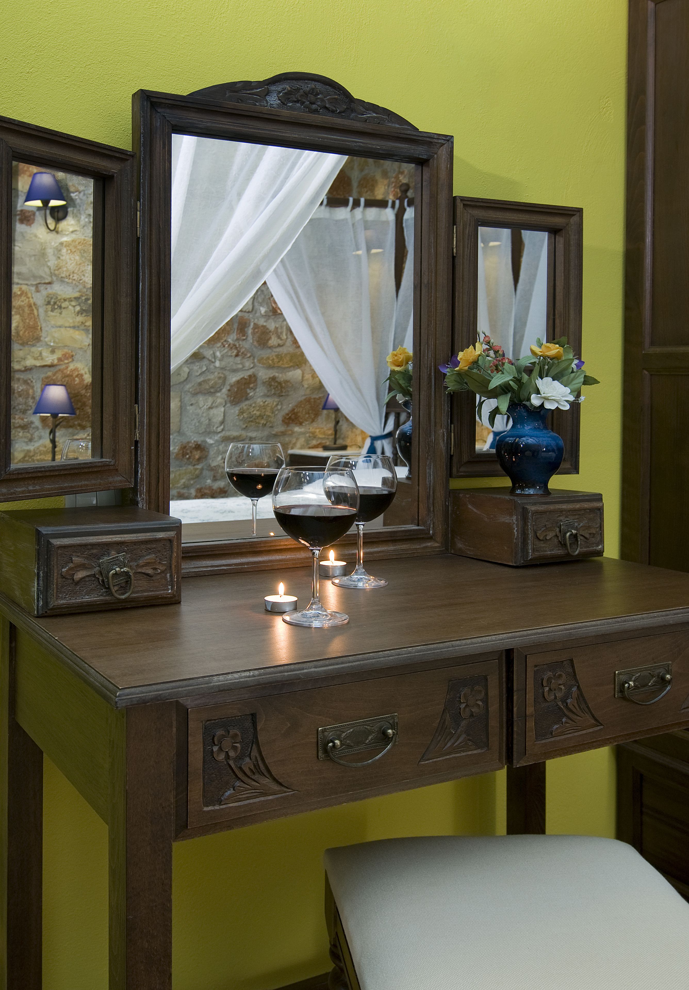 A wooden dresser with two mirrors, a vase with flowers, and two wine glasses with candles.